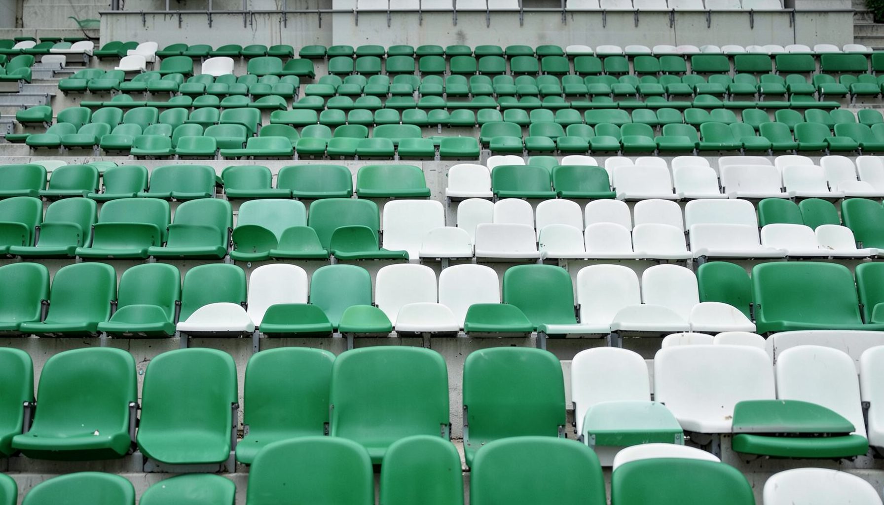 Stadium seats in alternating green and white rows, empty and quiet, soft diffused daylight