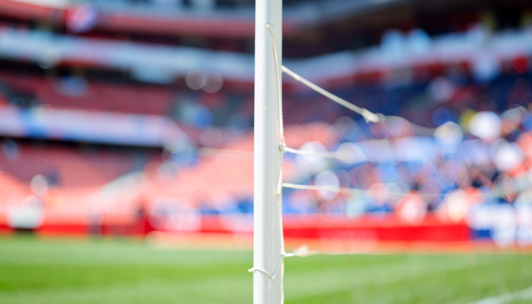Close shot of a corner flag with stadium seating blurred in background, crisp daylight, red and white accents