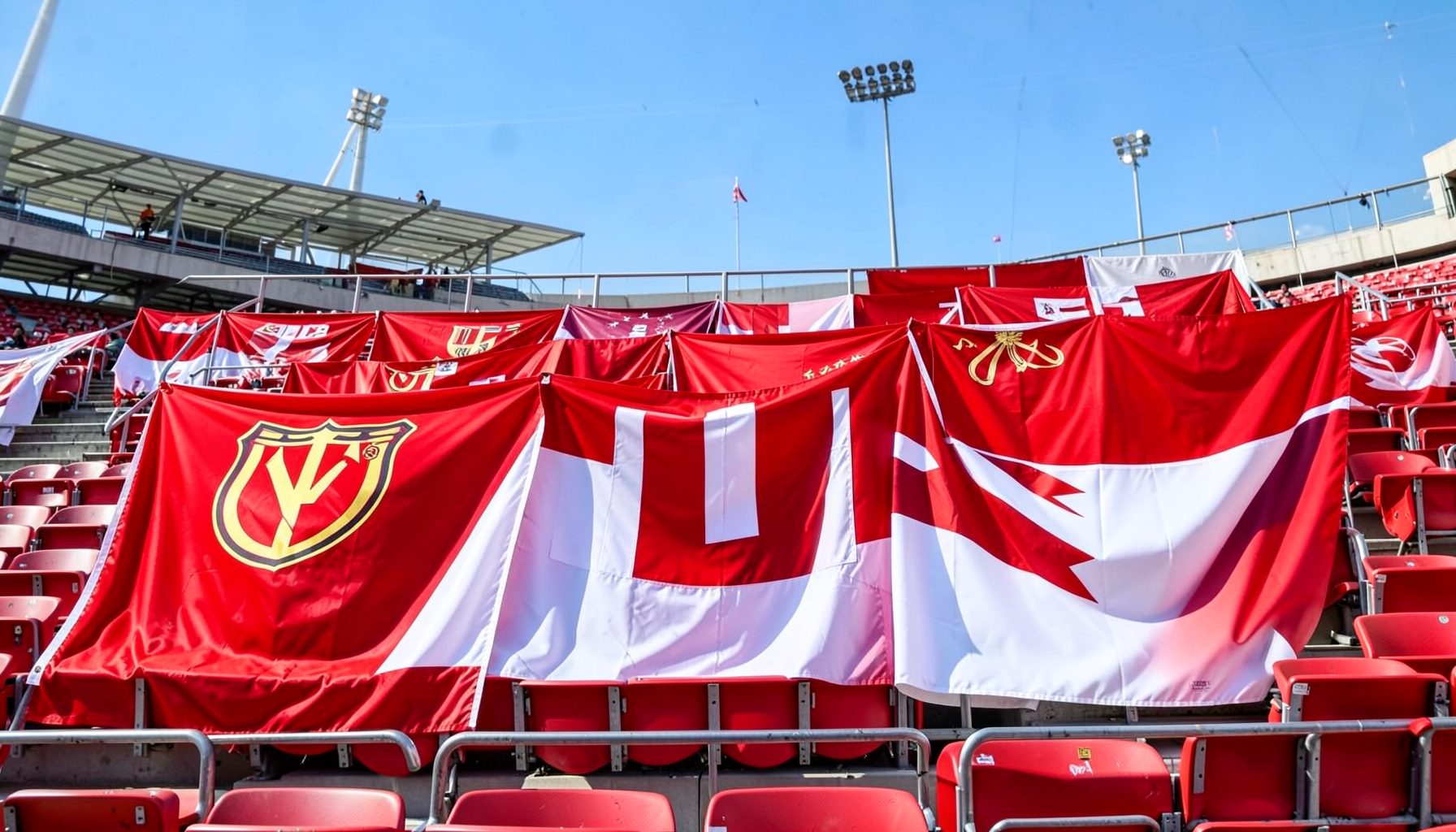 Two national team flags draped over stadium seats, vivid red and white against a bright afternoon sky